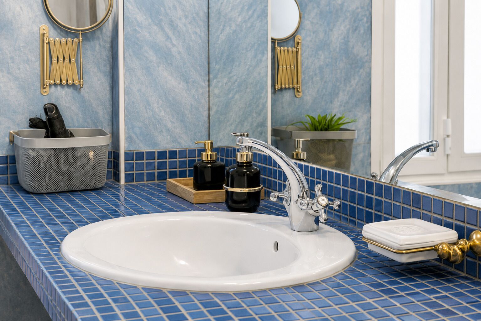 A bathroom with a white sink, blue tiled backsplash, gold fixtures, and a mirror.