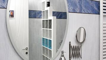 Un baño con un espejo redondo, una repisa de vidrio con artículos de aseo, un perchero y un radiador.
