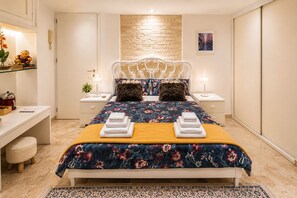 A modern bedroom with a bed, bedside tables, a desk, and a decorative wall.