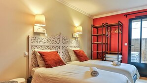 A double bed with white bedding and two red pillows, a wooden headboard with intricate carvings, and a red wall with a black-framed window. - Floreal : Villa 1900 au Coeur de St Gilles (Saint-Gilles-Croix-de-Vie)