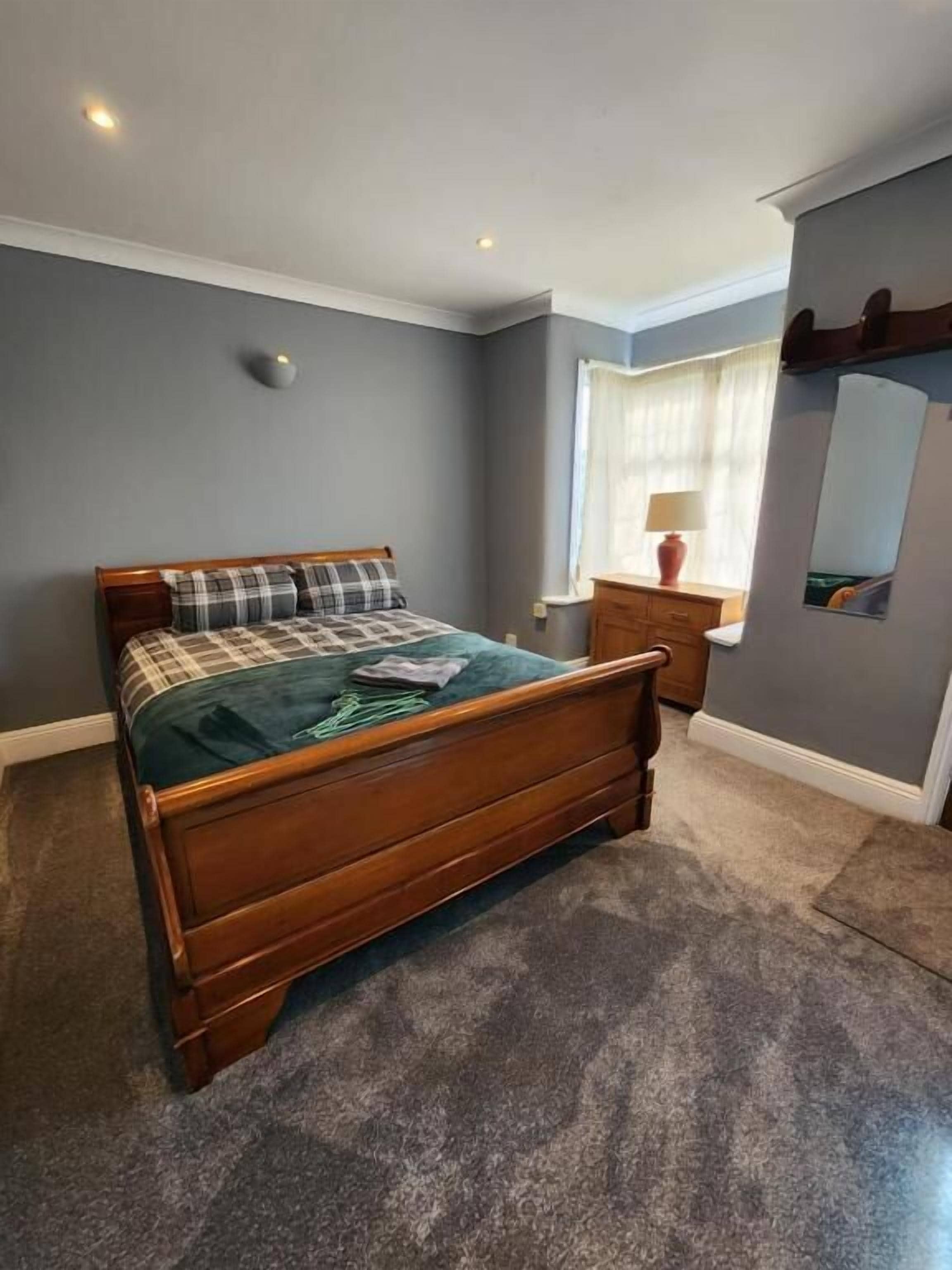A bedroom with a wooden bed, a nightstand, a mirror, and a window with curtains.