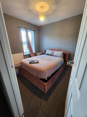 A bedroom with a bed, a window with curtains, and a radiator. - The Ivy (Grays)