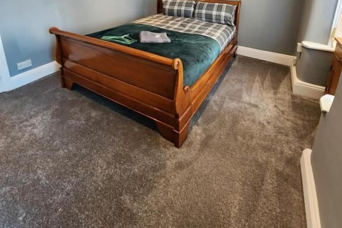 A bedroom with a wooden bed, a carpeted floor, and a light blue wall.
