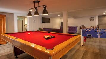 A pool table with a red felt surface and a cue ball, a purple sofa, and a blue table tennis table with a net.