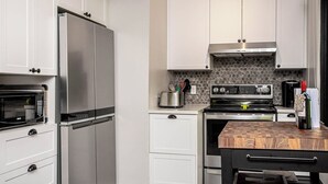 A modern kitchen with stainless steel appliances, white cabinetry, and a herringbone-patterned backsplash.