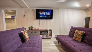 A living room with two purple sofas, a flat-screen TV, and a wooden cabinet with books and decorative items.