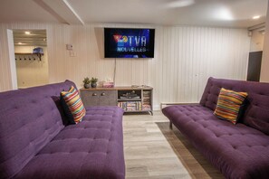 A living room with two purple sofas, a flat-screen TV, and a wooden cabinet with books and decorative items.