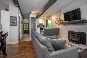 A modern living room with a fireplace, a flat-screen TV mounted above it, and a seating area with a sofa and chairs.
