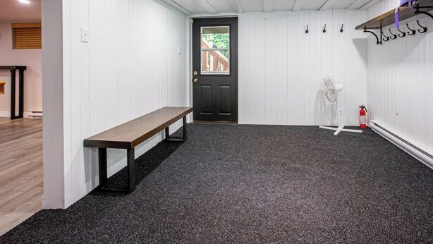 A hallway with a bench, a door, a fan, and a fire extinguisher.