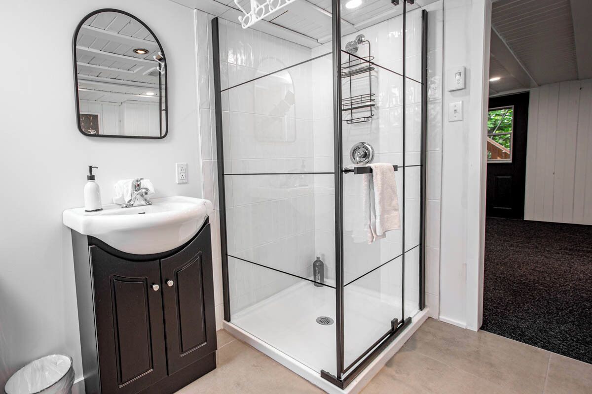 A bathroom with a glass-enclosed shower, a sink with a dark cabinet, and a mirror on the wall.