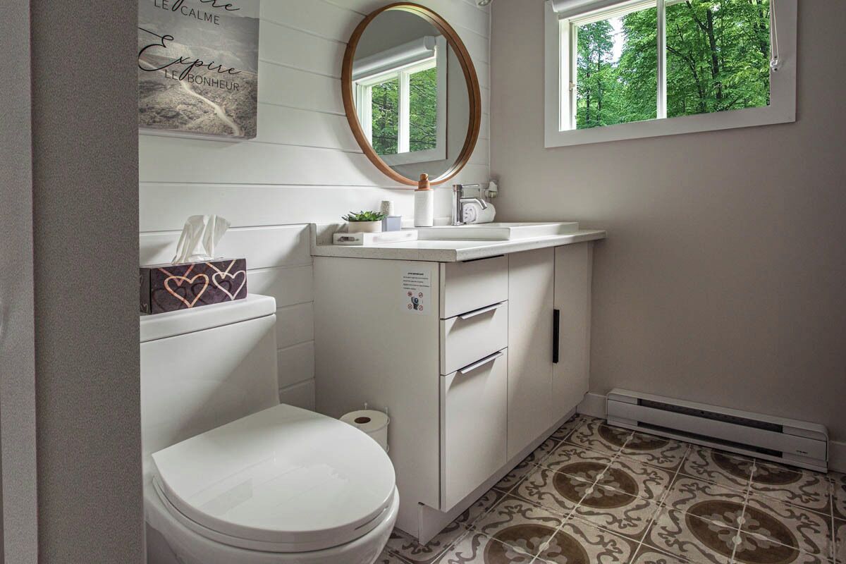 Une salle de bain comprenant des toilettes, un lavabo, un miroir et une fenêtre donnant sur des arbres.