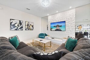 Un salon moderne doté d’un grand téléviseur à écran plat, de sièges confortables et d’œuvres d’art accrochées aux murs.