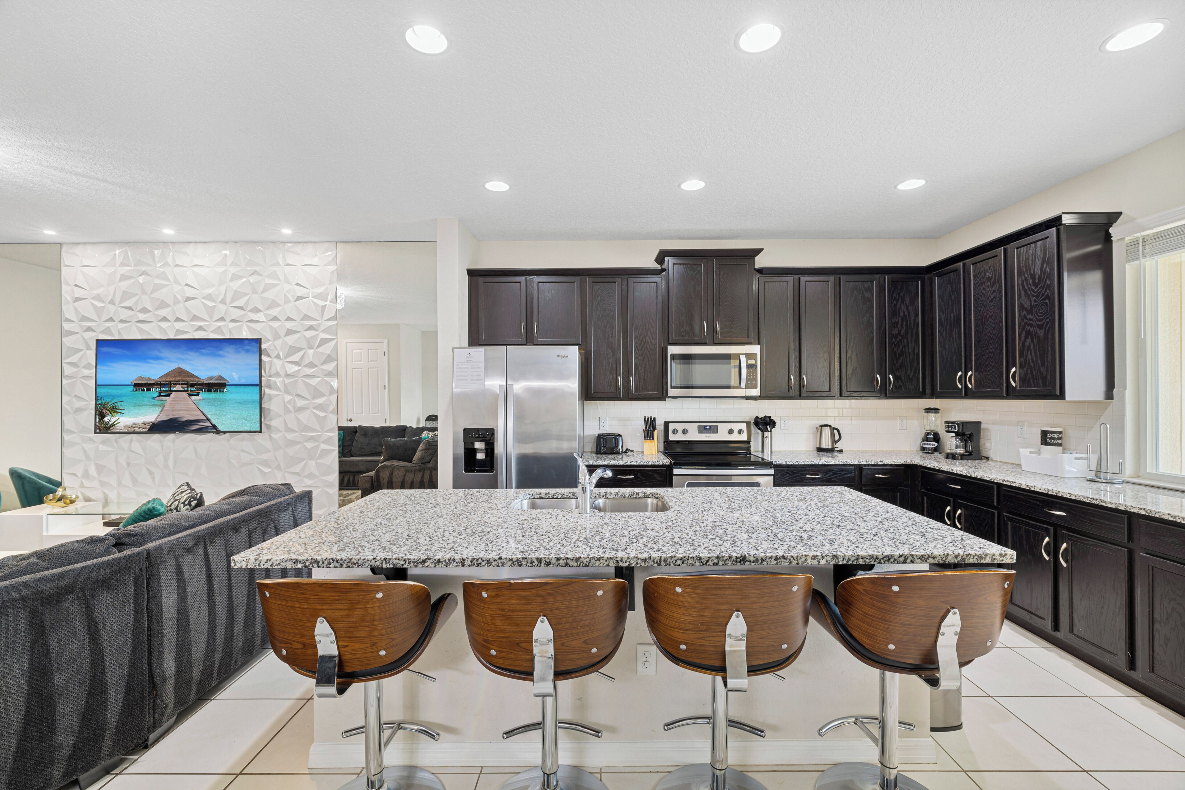 A modern kitchen with a granite island, dark wood cabinets, stainless steel appliances, and a seating area with bar stools.