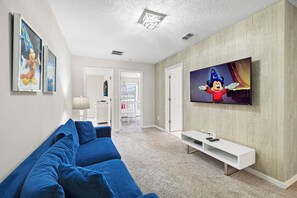 Ein Wohnzimmer mit blauem Sofa, einem flachbildfernseher an einer Holzwand und einer Tür, die auf einen Balkon führt.