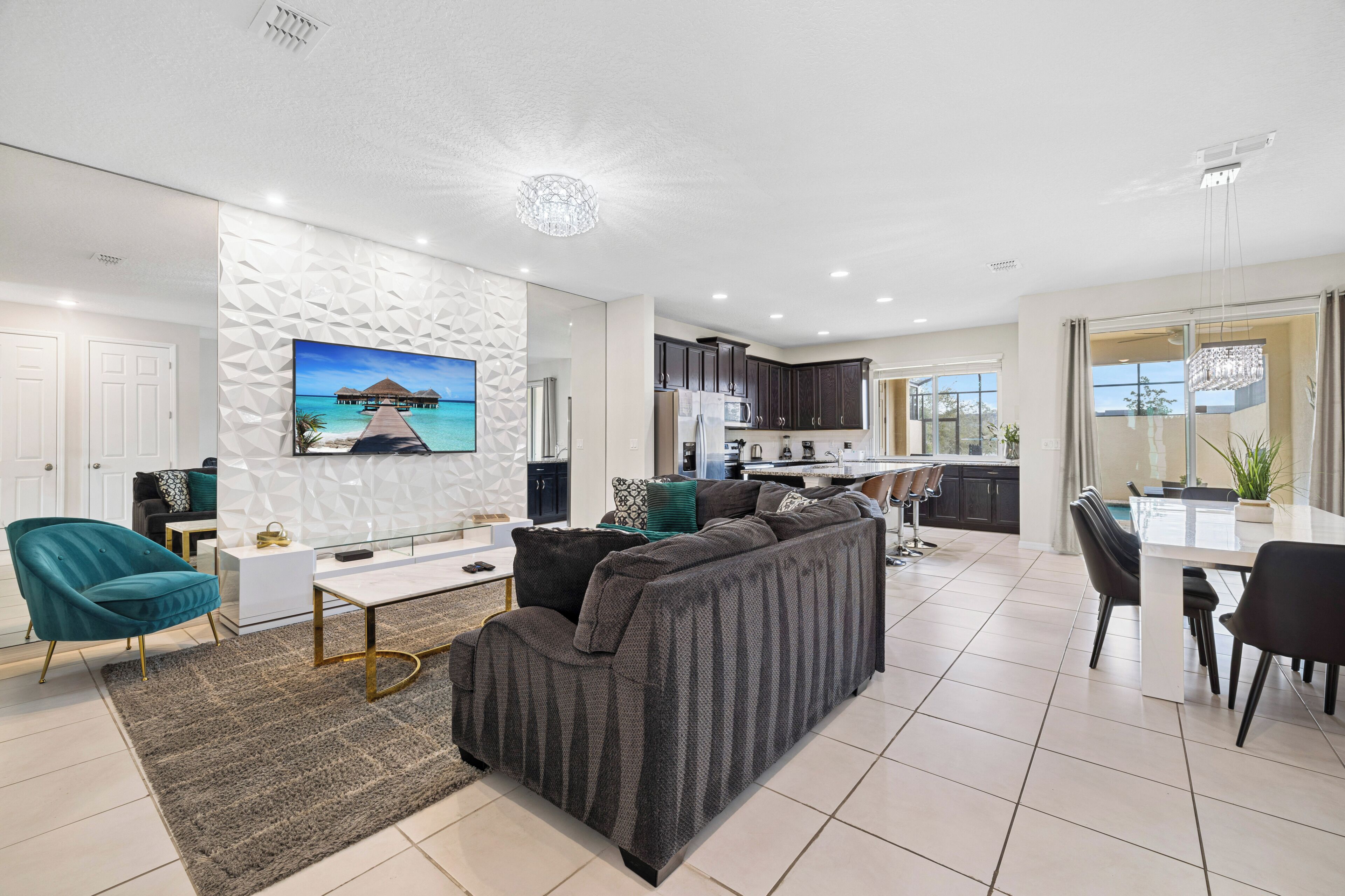 A modern living room with a sofa, a TV mounted on the wall, and a kitchen in the background.