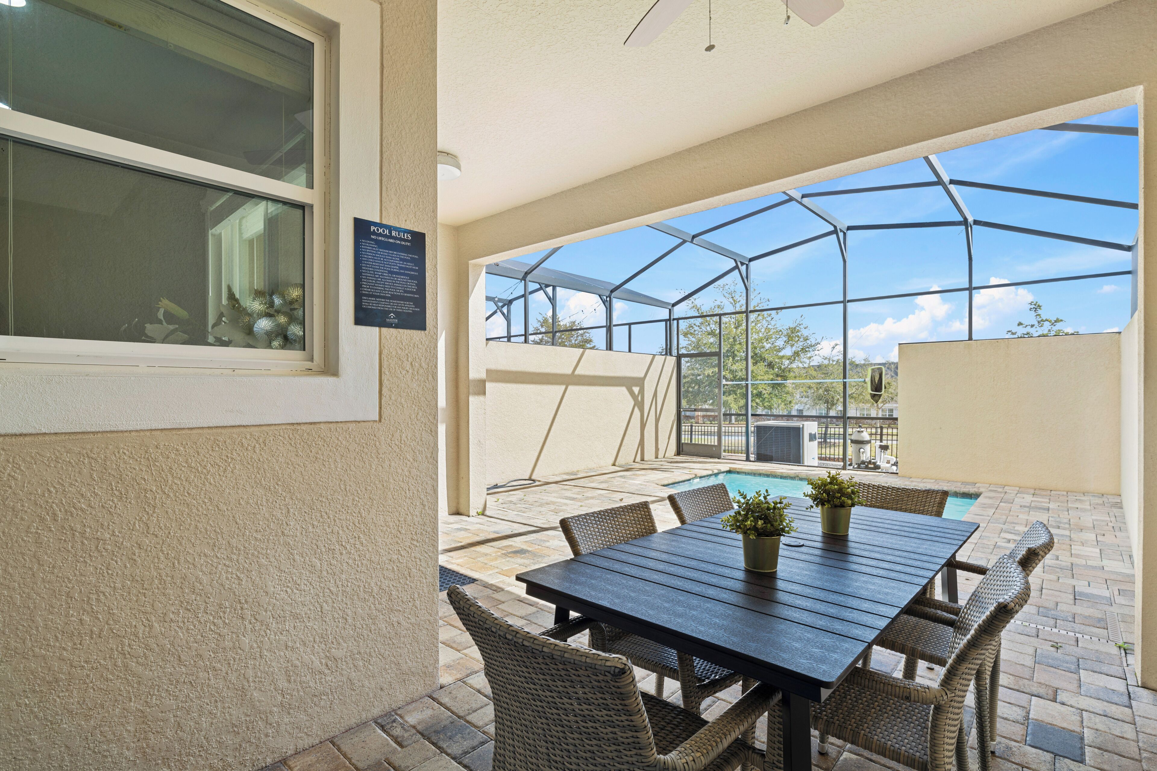 Ein überdachter Patio-Bereich mit Tisch und Stühlen, ein Schwimmbad und Blick auf den Himmel.