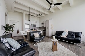 Ein modernes Wohnzimmer mit einer schwarzen Ledersofa, einem Essbereich mit einem weißen Stuhl, einer Küche mit weißen Schränken und einem Deckenventilator.
