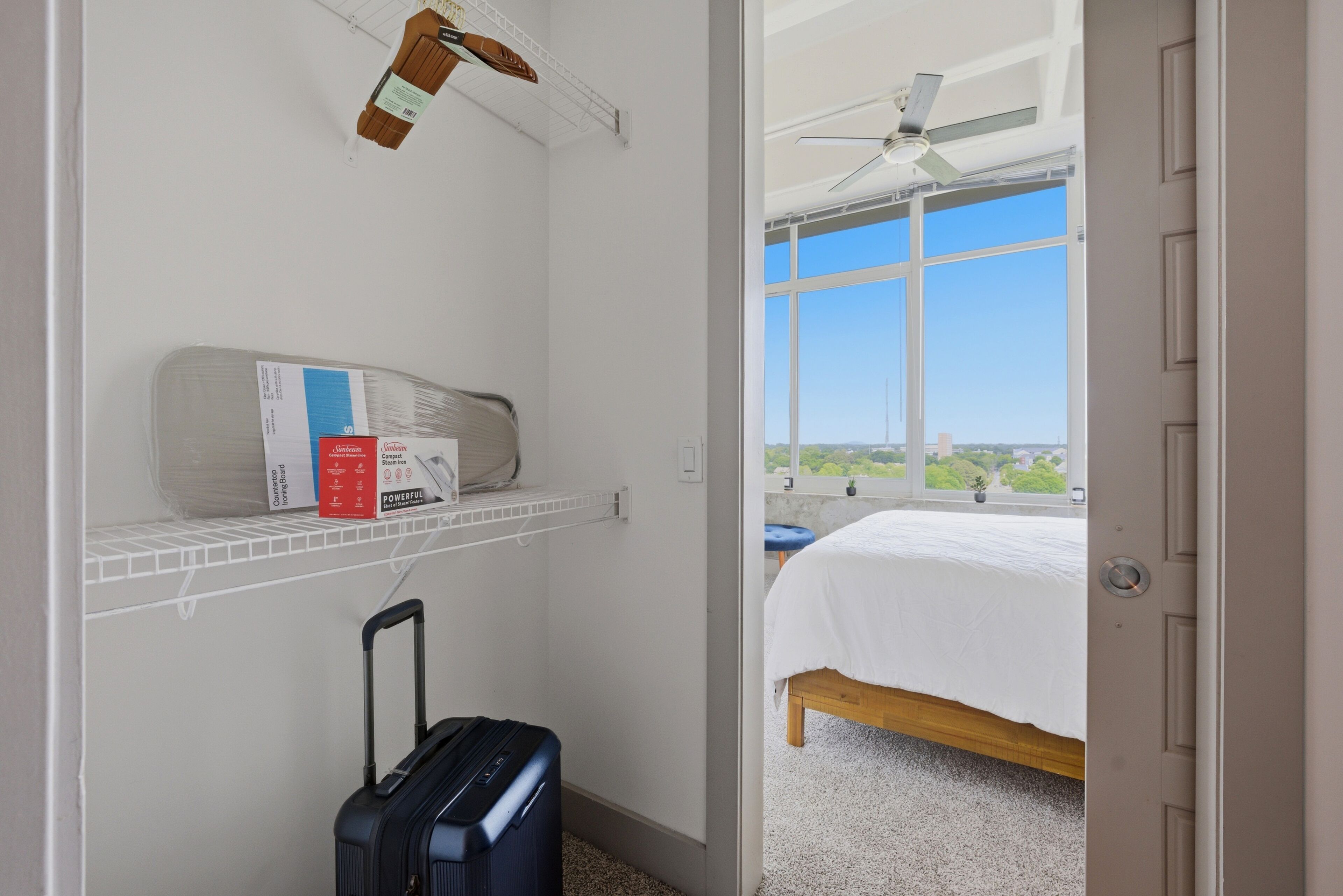 Ein Schlafzimmer mit Bett, Koffer, einem Regal mit Gegenständen, einem Fenster mit Blick und einem Deckenventilator.