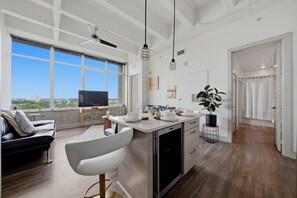 Eine moderne Küche mit einer großen Kochinsel, einem Essbereich mit einem weißen Stuhl und Blick auf die Stadt durch große Fenster.
