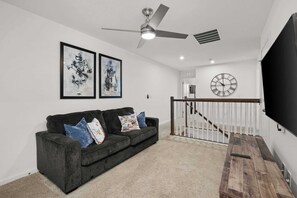 A modern living room with a dark grey sofa, a ceiling fan, and a mounted clock. - Disney Retreat w/ Private Pool & Resort Access (Kissimmee)
