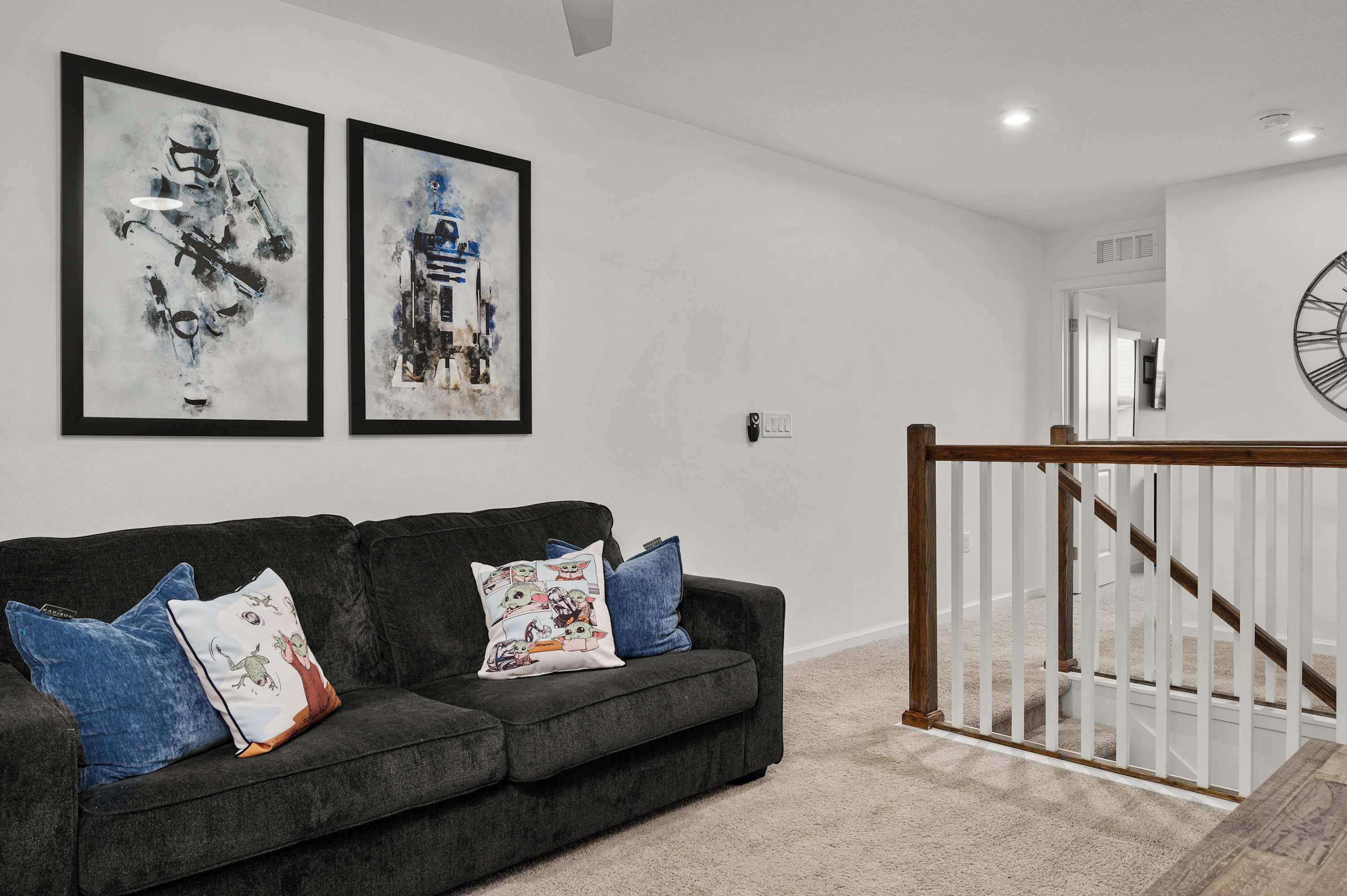 A modern living room with a dark grey sofa, multiple cushions, and two abstract paintings on the wall.