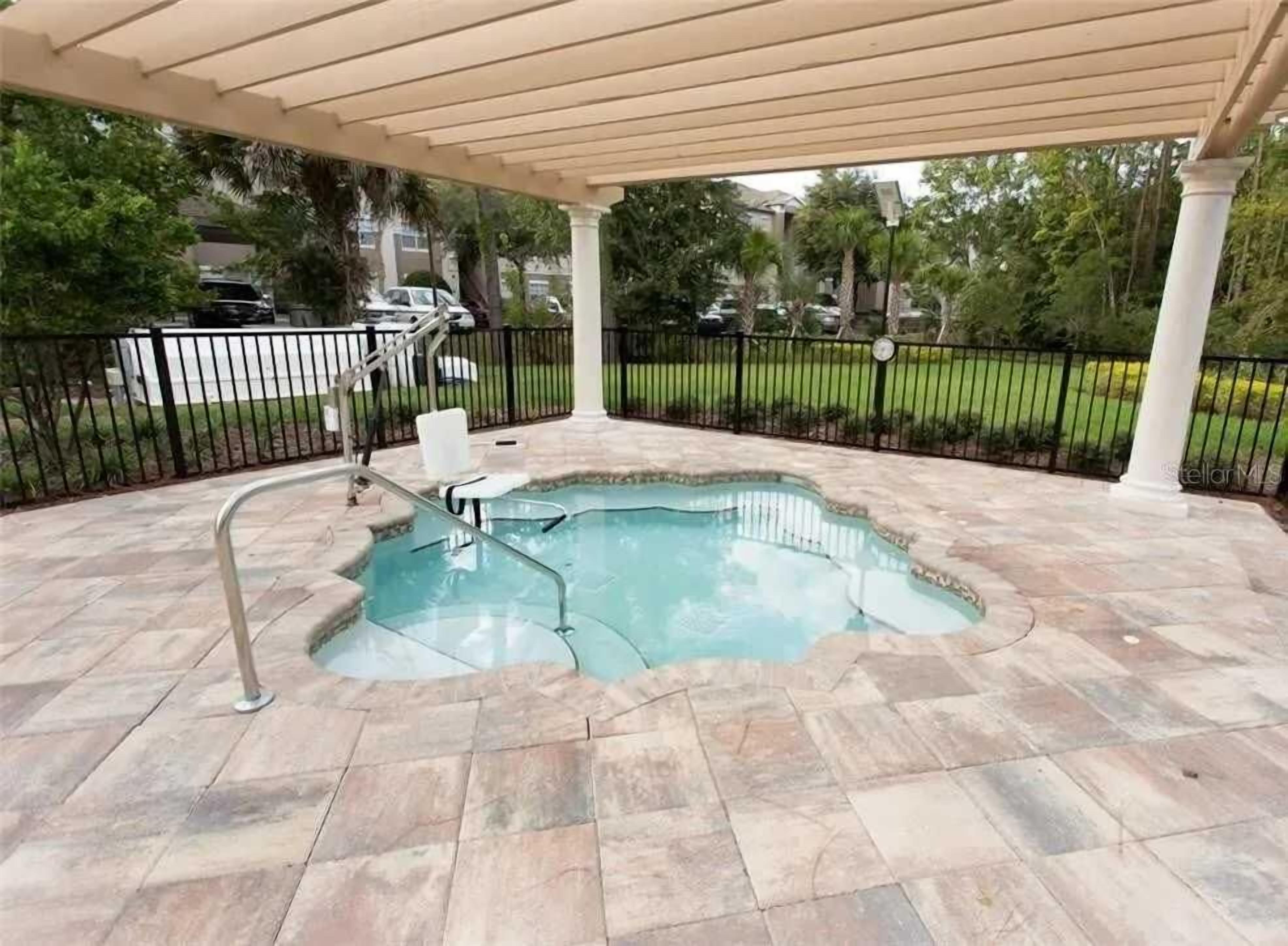 A covered swimming pool with a curved edge, surrounded by stone tiles, and a metal railing.