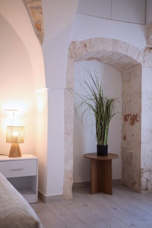 Une pièce avec une table de chevet blanche, une lampe, une plante en pot et un arc en pierre.