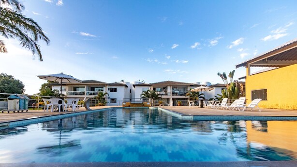 A swimming pool with lounge chairs and umbrellas, surrounded by multi-story buildings with balconies. - Beautiful Apartment 130m From the Beach Mut0054 (Porto Seguro)