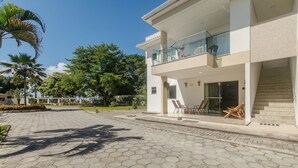 A modern two-story building with a balcony, a paved courtyard, and surrounding greenery. - Beautiful Apartment 130m From the Beach Mut0054 (Porto Seguro)