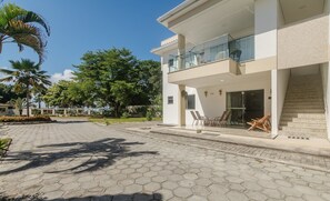A modern two-story building with a balcony, a paved courtyard, and surrounding greenery. - Beautiful Apartment 130m From the Beach Mut0054 (Porto Seguro)