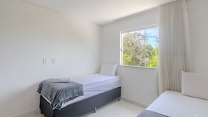 A bedroom with a bed, a bedside table, a window with curtains, and a view of trees. - Apartment With Barbecue. in Cond. w/ Pool Mut0056 (Porto Seguro)