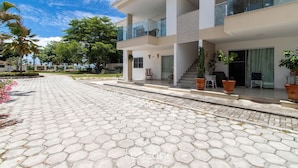 A modern two-story building with a hexagonal tile driveway, outdoor seating, and potted plants. - Apartment With Barbecue. in Cond. w/ Pool Mut0056 (Porto Seguro)