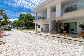 A modern two-story building with a hexagonal tile driveway, outdoor seating, and potted plants. - Apartment With Barbecue. in Cond. w/ Pool Mut0056 (Porto Seguro)