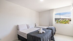 A hotel room with two beds, a window with a view of buildings and greenery, and a ceiling light. - Apartment With Barbecue. in Cond. w/ Pool Mut0056 (Porto Seguro)