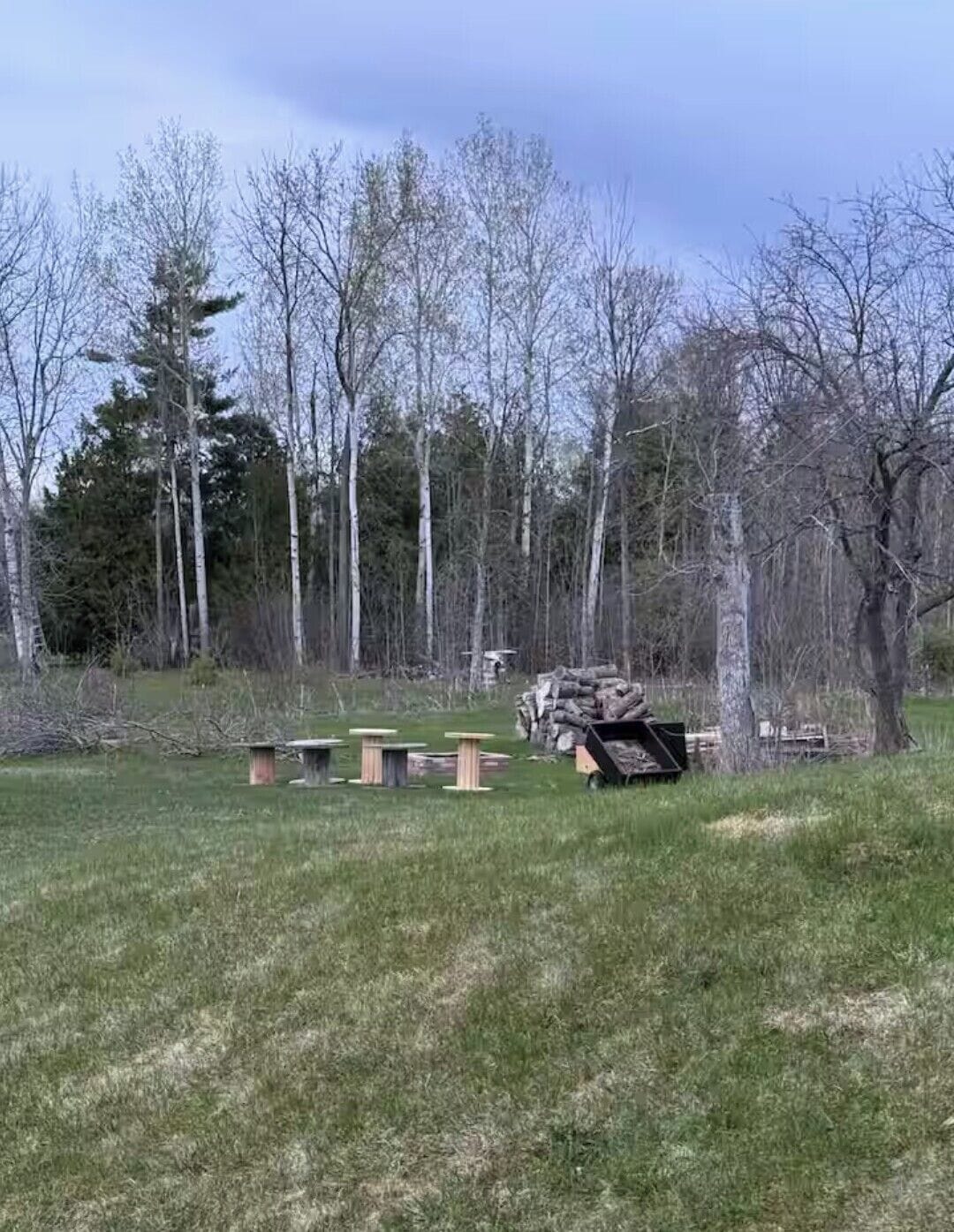 Un campo cubierto de hierba con varias estructuras de madera, posiblemente mesas de picnic, y una carretilla.