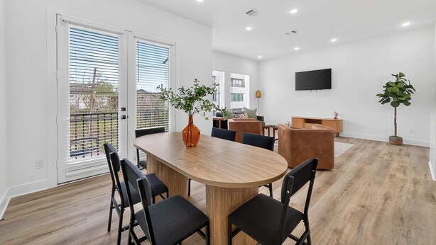 Un salon moderne avec un coin repas, comprenant une table en bois, des chaises noires, un canapé et un téléviseur fixé au mur.