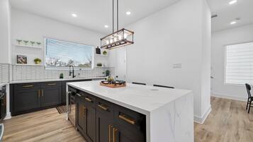 A modern kitchen with a central island, dark cabinetry, and a pendant light.