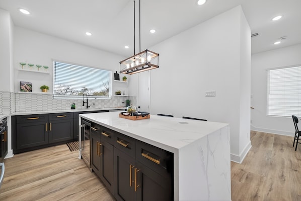 A modern kitchen with a central island, dark cabinetry, and a pendant light.