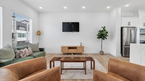 Un salon moderne avec un téléviseur à écran plat, une table basse en bois et un canapé vert.