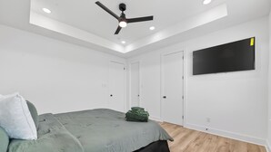 Une chambre à coucher comprenant un lit, un ventilateur de plafond, des spots encastrés, un téléviseur à écran plat et une armoire.