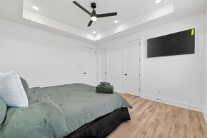 Une chambre à coucher comprenant un lit, un ventilateur de plafond, des spots encastrés, un téléviseur à écran plat et une armoire.