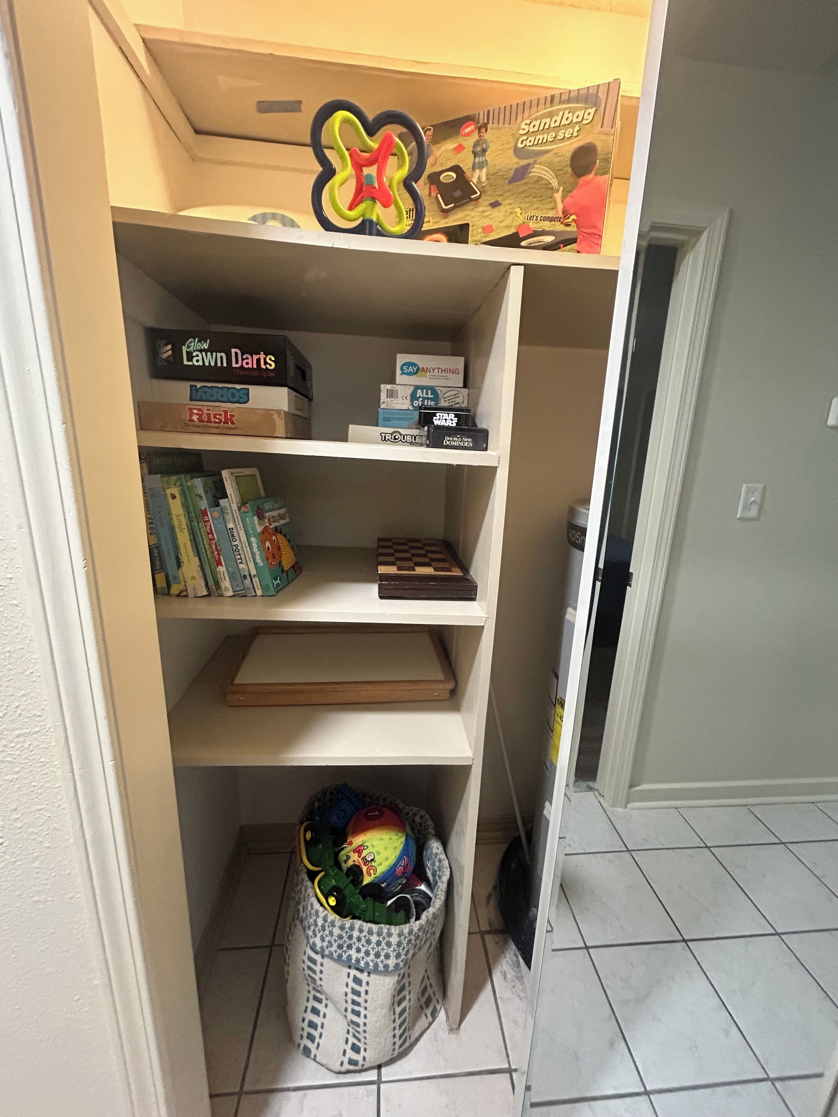 A storage area with shelves containing various items including board games, books, and a basket with toys.