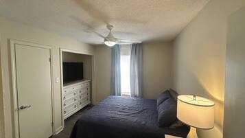 A bedroom with a bed, a dresser, a television, and a ceiling fan.