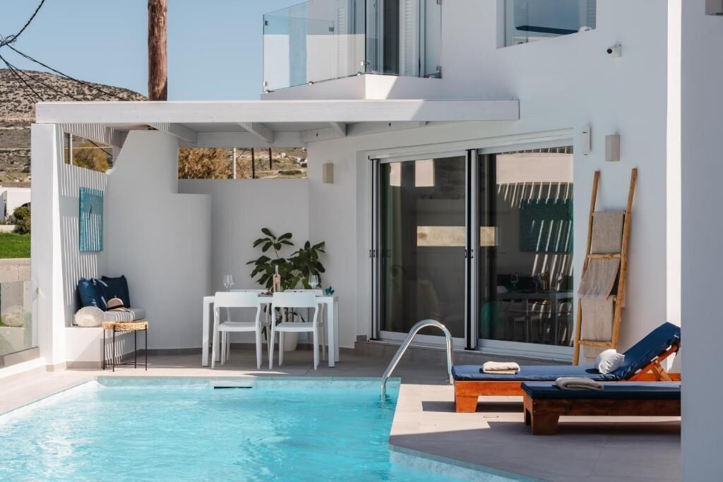 A modern outdoor pool area with a glass balustrade, a dining table with chairs, and lounge chairs.