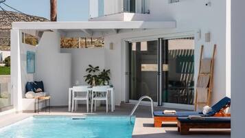 A modern outdoor pool area with a glass balustrade, a dining table with chairs, and lounge chairs.