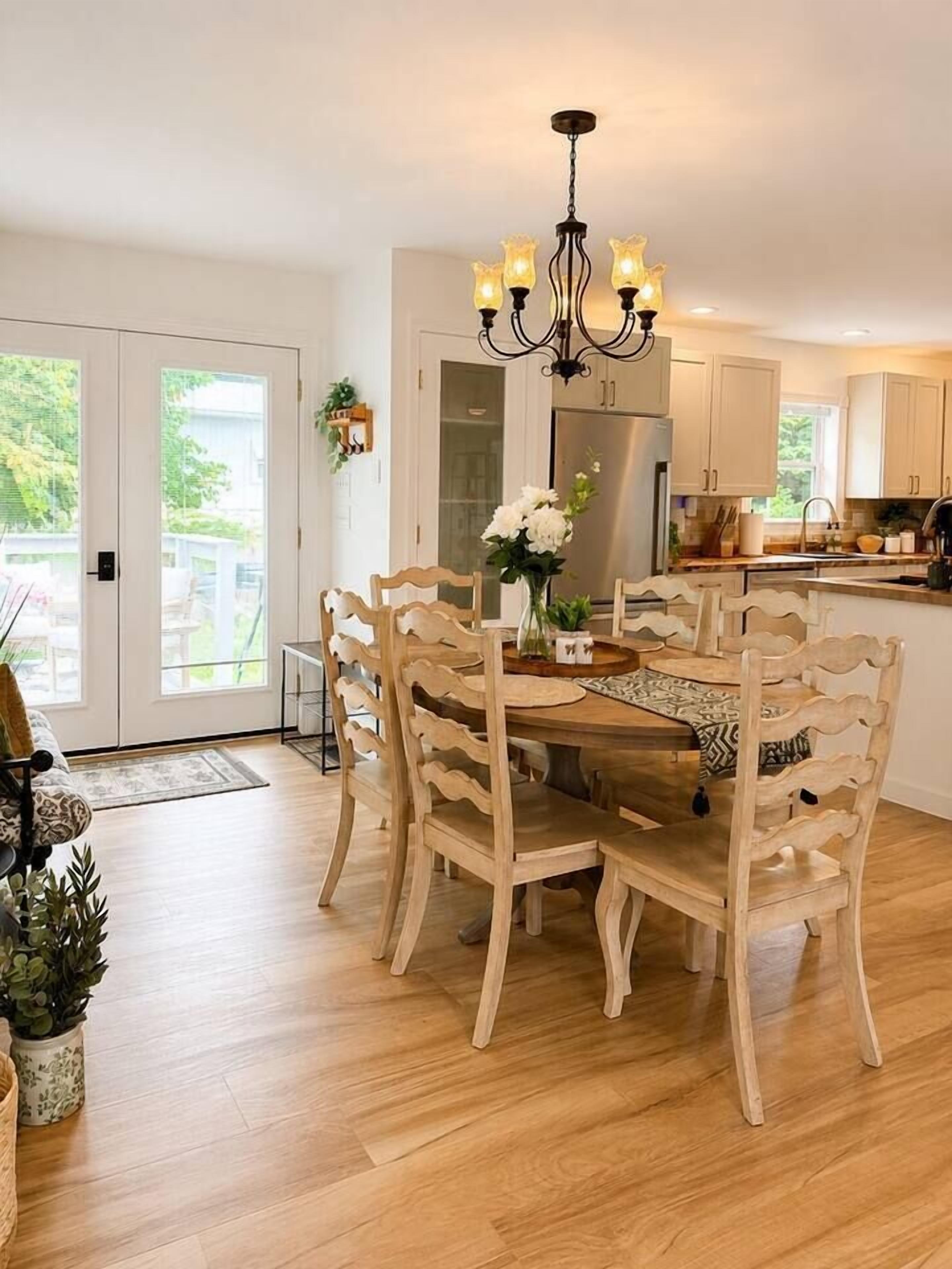 A dining area with a wooden table and chairs, a chandelier, and a view of the outdoors.