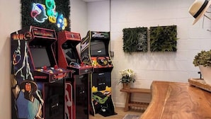 Een kamer met drie speelautomaten, een houten tafel en een plant aan de wand.