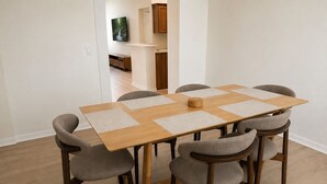 Een eettafel met zes stoelen, een televisie aan de muur en een keuken in de achtergrond.