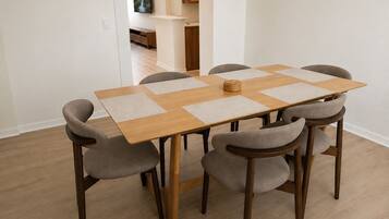 A dining table with six chairs, a television mounted on the wall, and a kitchen area in the background.