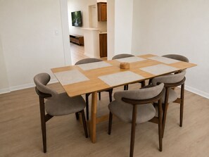 A dining table with six chairs, a television mounted on the wall, and a kitchen area in the background. - Sand and Sage: 3BR, 2BH, Heated Pool, Fenced Yard (Spring Hill)
